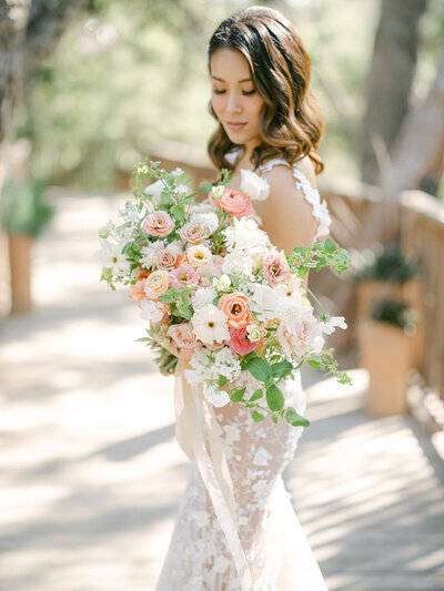 Kohnur bride with soft romantic curls and glowing natural makeup holding pastel bouquet in garden wedding