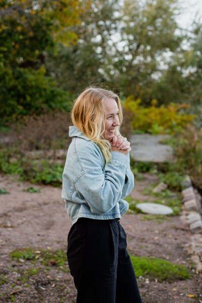 mielen paremminvoinnin ja kehomieliyhteyden valmentaja  seisoo luonnon keskellä ja katsoo käden ristittyinä eteenpäin hymyillen