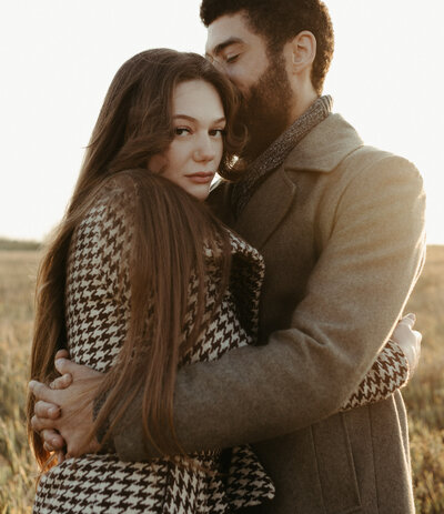 Couples editorial session at Northeast Swale, Saskatoon. Livia looking at camera while Sam kisses her with his eyes closed.