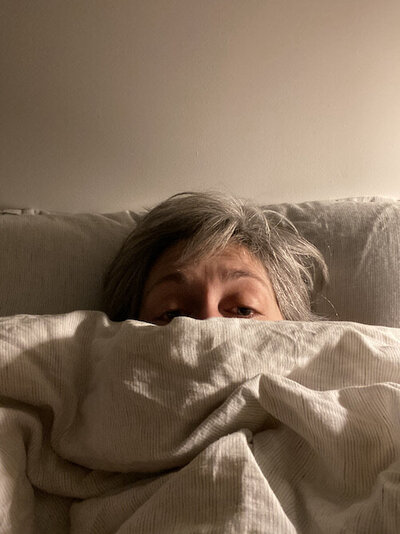 A picture of Sally hiding under a duvet, her eyes and hair visible, looking insecure
