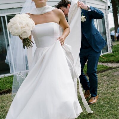bride in wedding dress holding bouquet while groom lifts train behind her image by minnesota photographer tom thornton