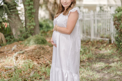 Pregnant mother in white dress with hands on her baby bump by Maternity Photographer Greenville SC.