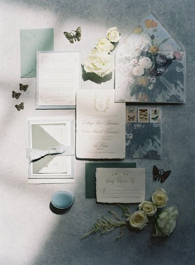 Romantic wedding flat lay with fine art invitations, soft ivory florals, vintage stamps, and butterfly details styled by Kaytlyn Rei Photography in Richmond, VA.