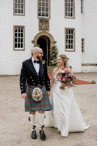 A close photography of a couple as they walk hand in hand down the aisle after their outdoors Glen Tanar wedding ceremony.
