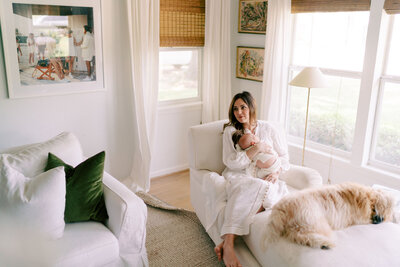Mom in a white dress sitting in a white chair holding her newborn on her chest