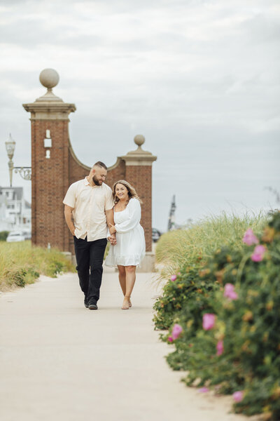 Spring Lake | Couple walking by pink flowers during summer engagement photo | New Jersey