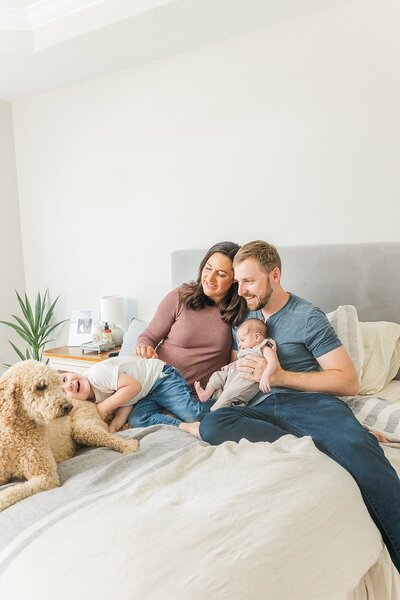 family sits on bed  during in home newborn photo session with Sara Sniderman Photography in Metro West Boston Massachusetts