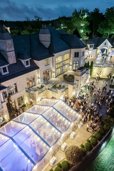 Aerial view of an outdoor wedding reception with a clear tent and glowing lights at a large estate.