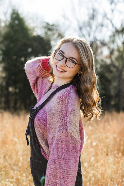 Girl playfully posing in front of a field wearing a color pink sweater