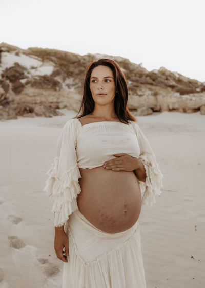A mum gently rests her hand on her bump at a Mullaloo beach in Perth