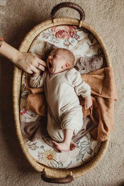 newborn baby in basket holding mums hand yawning