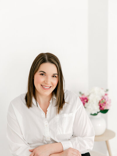 Headshot of a woman in a white blouse with a vase of flowers behind her on a table