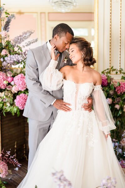 A groom holds his bride as she smiles and gently touches his jawline