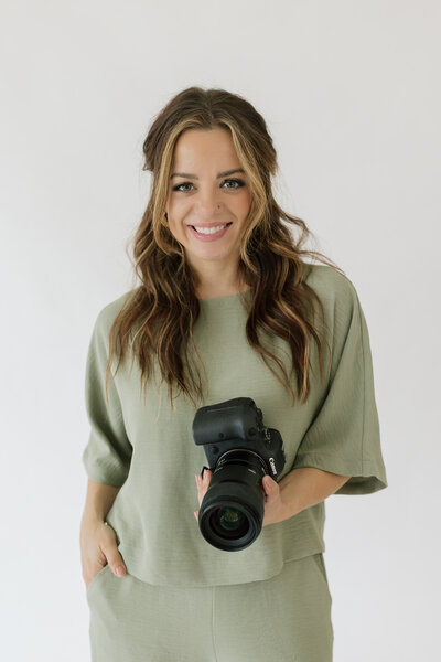 Headshot of photographer  Charity White , posing in a seated position, smiling, and holding a camera