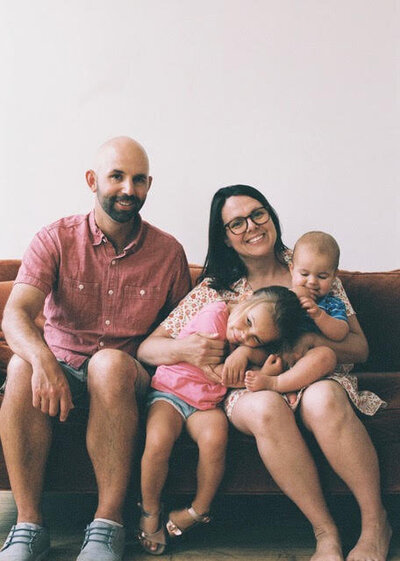 A therapist family joyfully sits on a couch, cuddling their baby, creating a warm and loving atmosphere.