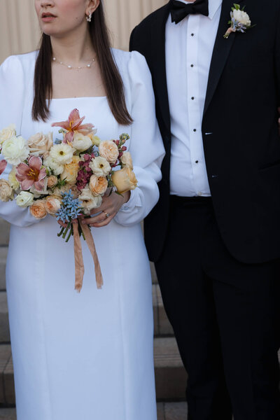 bride and groom holding flowers and looking away from camera