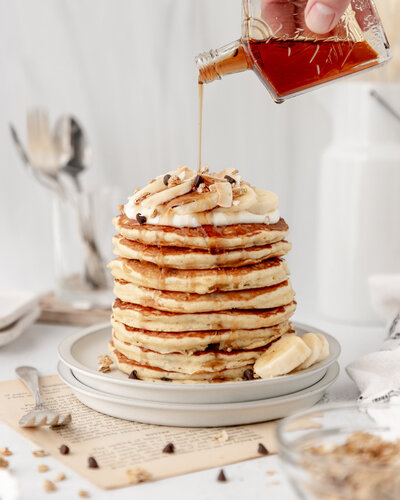 maple syrup being poured on a stack of pancakes