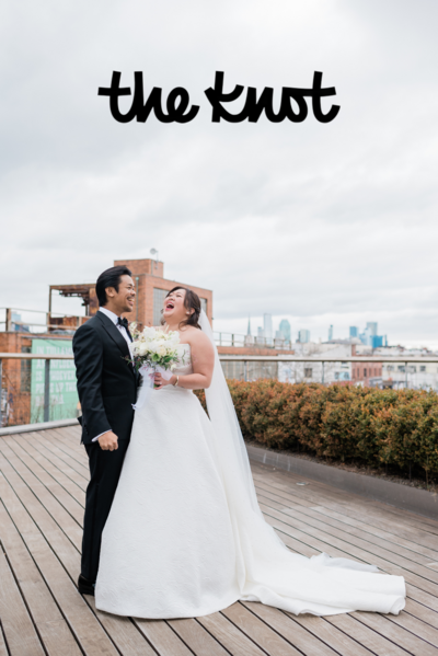 Bride and groom laugh together while stand on a city rooftop