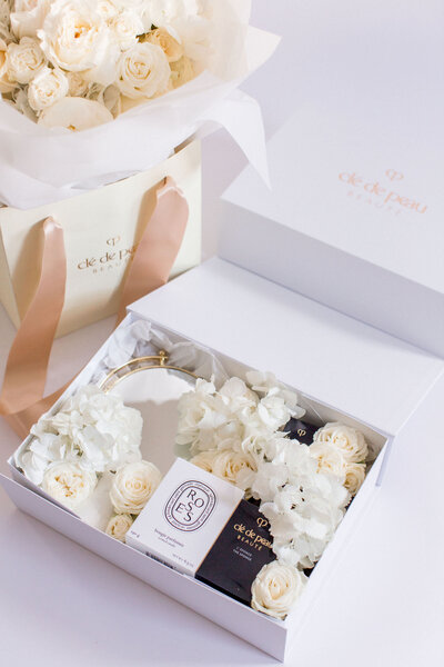 A Cle de Peau gift box with flowers,, a diptique candle and make up.