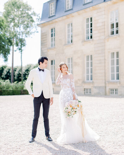 Wedding Couple standing in front of New England Estate Wedding Venue, bride tucking hair and looking off in the distance and the groom looking at the bride, photographed by New England Wedding Photographer Ashley Helen