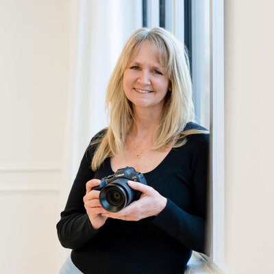 Woman with blonde hair wearing black top holding camera posing for photo