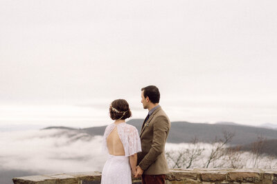 Bride and groom standing hand in hand with a mountain lake behind them during their intimate Virginia elopement, photographed in natural light and soft tones.

