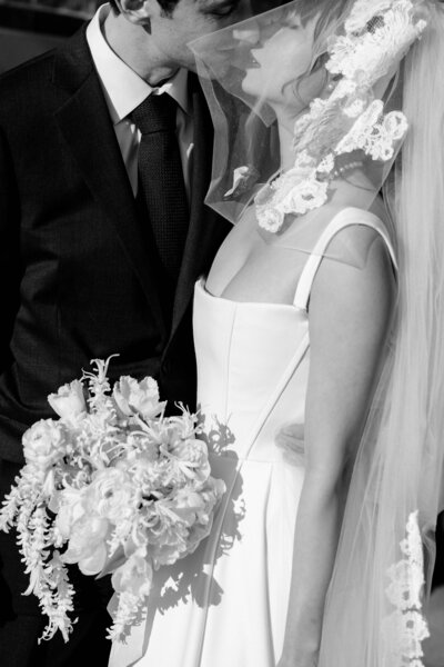 A close-up, black-and-white shot of bride and groom kissing under her veil