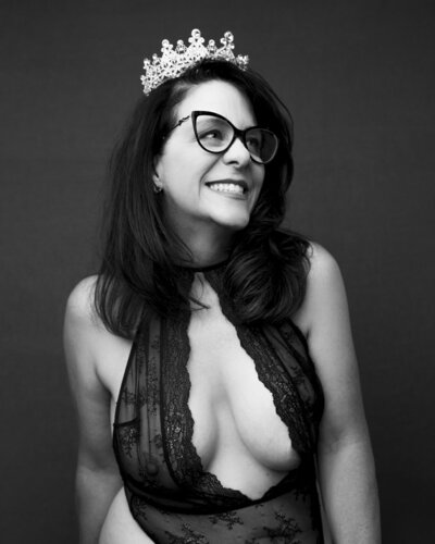 Black and white image of woman in a crown and lingerie posing for a boudoir portrait by Poplight photography