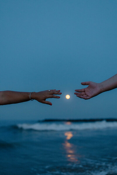 close up photo of hands with full moon on delaware beach during blue hour by sabrina leigh