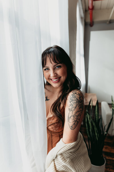 woman smiling behind curtain in boudoir studio 