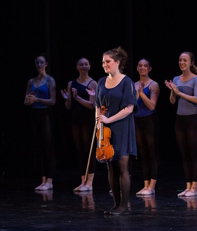 Violinist Erika Burns takes a bow in front of dancers onstage.