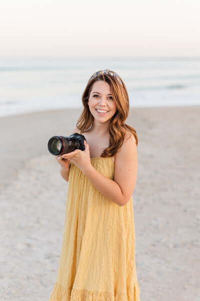 Woman holding a camera in a yellow dress on a beach