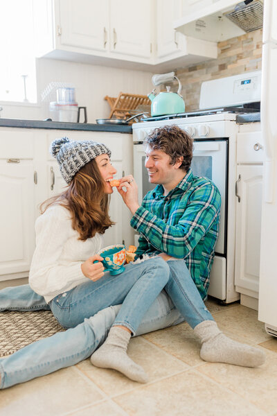 Best high school senior photographer in New Jersey. Photo of a couple sitting on the kitchen floor eating orange slices. The man is wearing flannel and the girl is wearing a winter beanie and a sweater.