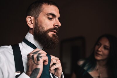 Le marié ajuste son noeud de cravate sous le regard de sa témoin lors des préparatifs de son mariage en Allier.