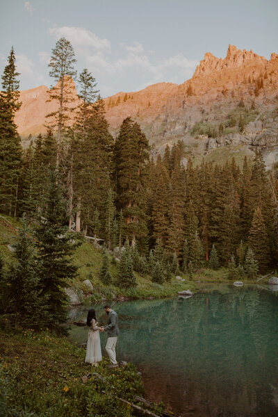 Couple stands on the edge of an alpine lake at sunrise in Telluride