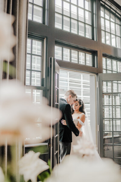 Bride and Groom hug and laugh surrounded by their bridal party. Bride has a flower crown and groom is in  a black tux. Anna Brace, a wedding photographer omaha nebraska