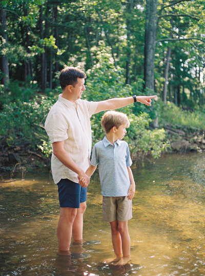 Father and son stand ankle deep in lake water gazing out ahead of them, while holding hands - captured on film by photographer Little Rock Bailey Feeler