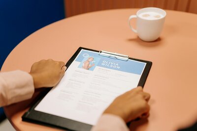 Person reviewing a resume on a clipboard next to a cup of coffee on a pink table.