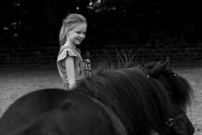 Vrolijk zelfverzekerd meisje met de voorgrond een zwarte pony in Midlaren.