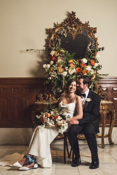 Newlyweds seated in front of a vintage mirror and lush floral display, enjoying an elegant indoor wedding planned in Austin, Texas.