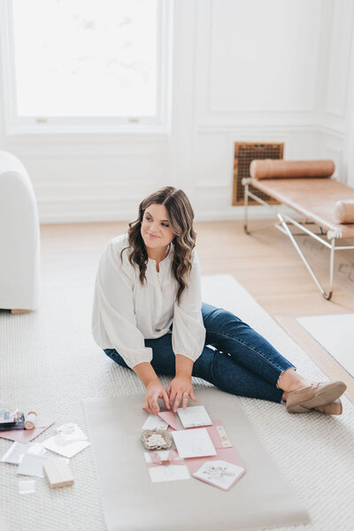 Heather, co-founder of Heather Paperie sitting on floor styling a flat lay photograph of a pink custom wedding invitation suite