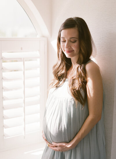 Maternity photography with mother indoors in a blue dress holding pregnant belly