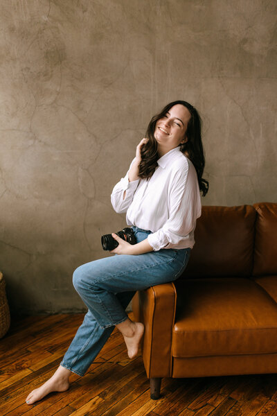 woman with camera sits on arm of couch