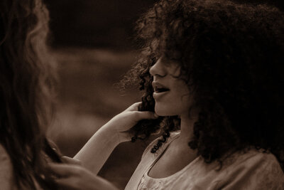 Woman with natural hair plays with her brides hair during the elopement by a family pond.