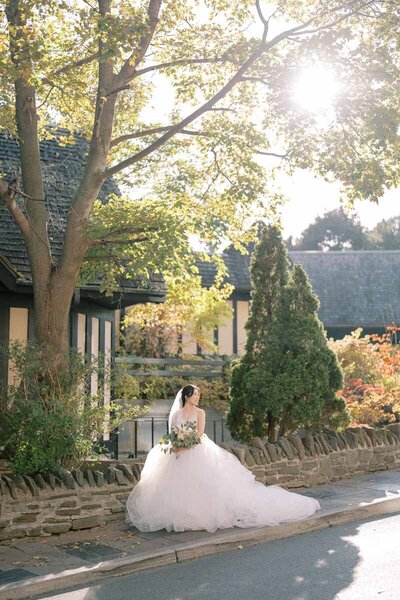 Bride in ballgown sitting on stone curb in afternoon light, dreamy editorial-style wedding portrait in Toronto