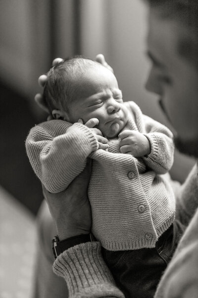 Newborn baby cradled in father’s arms during lifestyle photography session in South Florida.