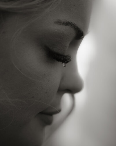 Close-up black and white portrait of a bride shedding a tear during her wedding ceremony, photographed by Rainstorm Photo & Video with a soft, emotional, documentary approach.