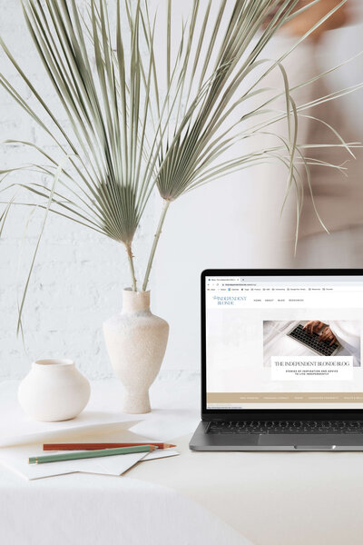 Laptop showing web page design for blogger on desk with ceramic vases