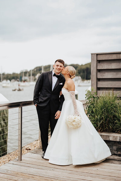 bride kissing groom on cheek standing on dock
