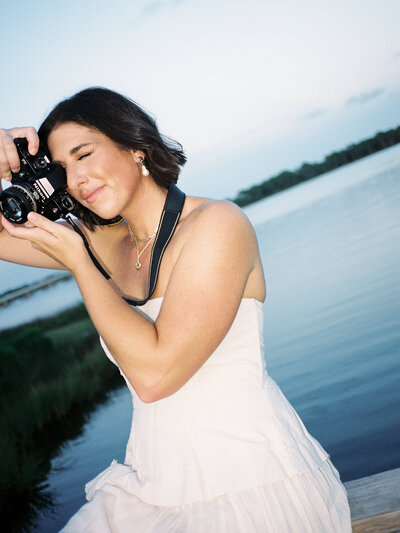 Flash film photo of Courtney Leigh in a white dress holding up a film camera